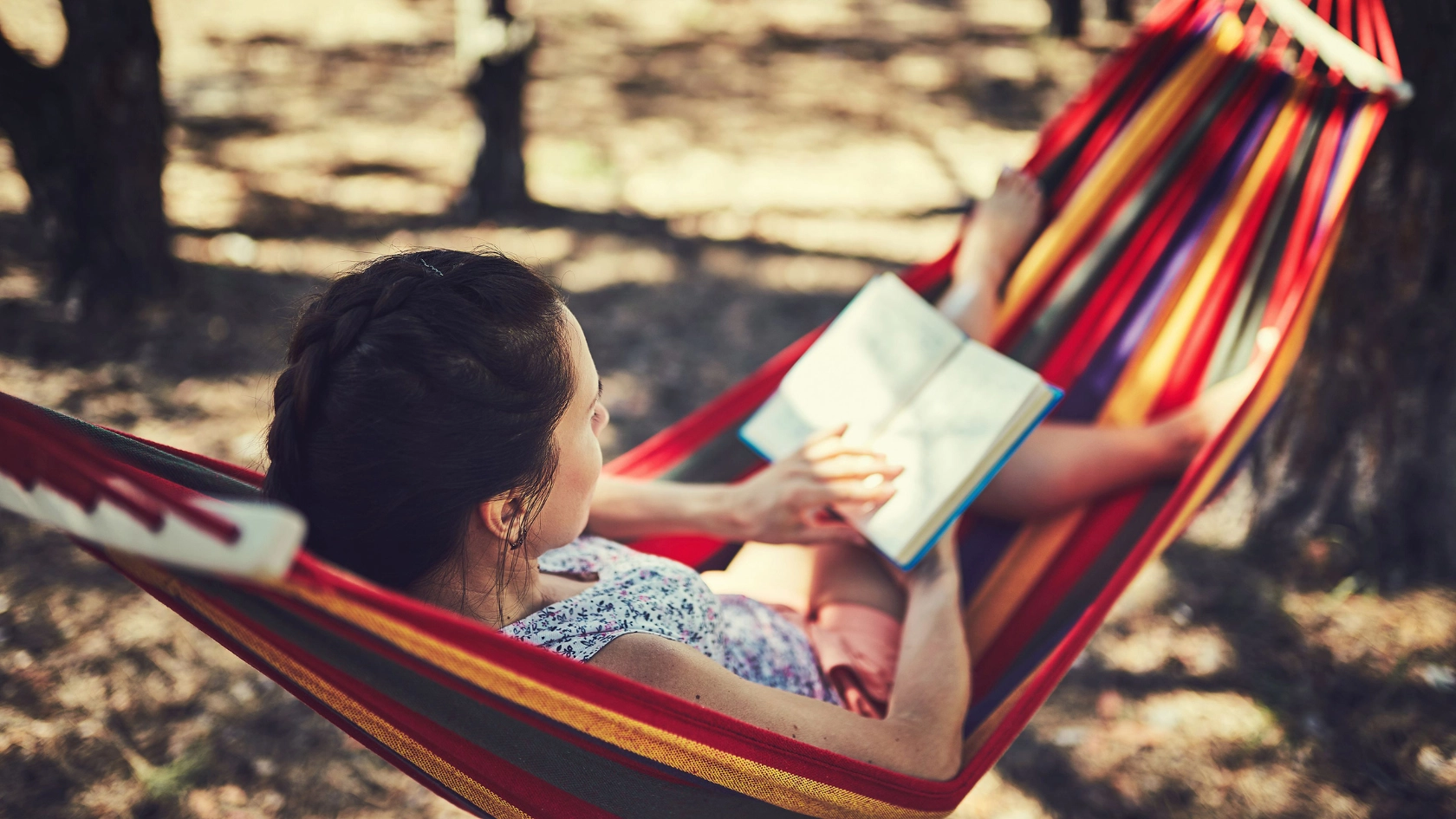Junge Frau liegt in einer Hängematte und liest ein Buch