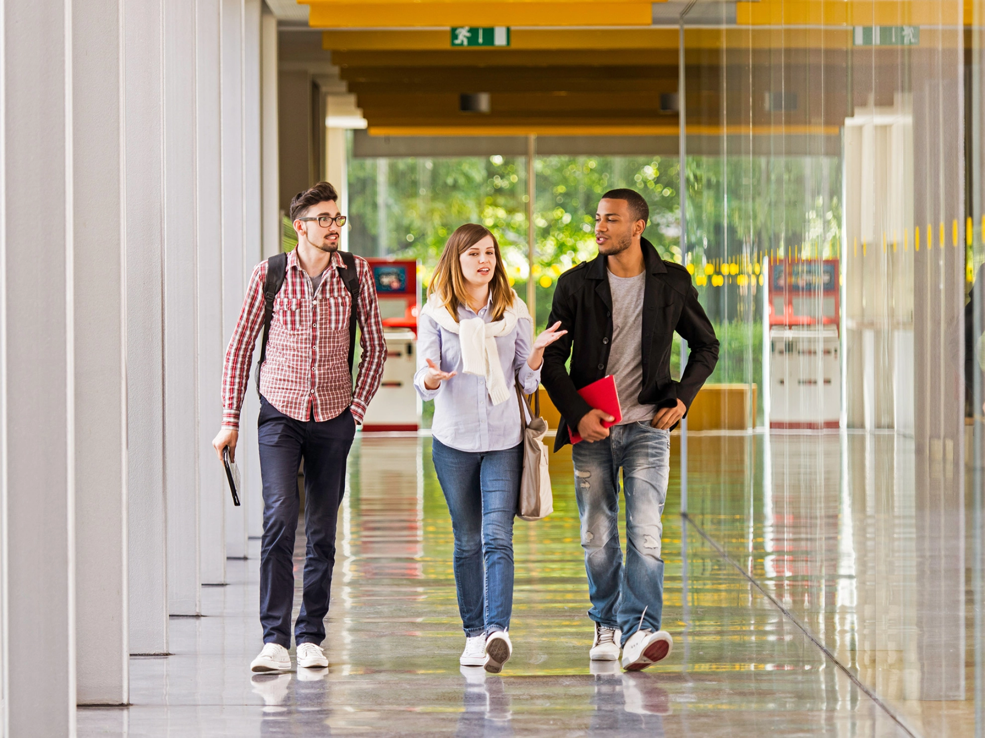 Eine Studentin und zwei Studenten laufen über einen Korridor und unterhalten sich dabei.