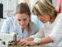 Ausbilderin zeigt einer Auszubildenden etwas an der Nähmaschine.